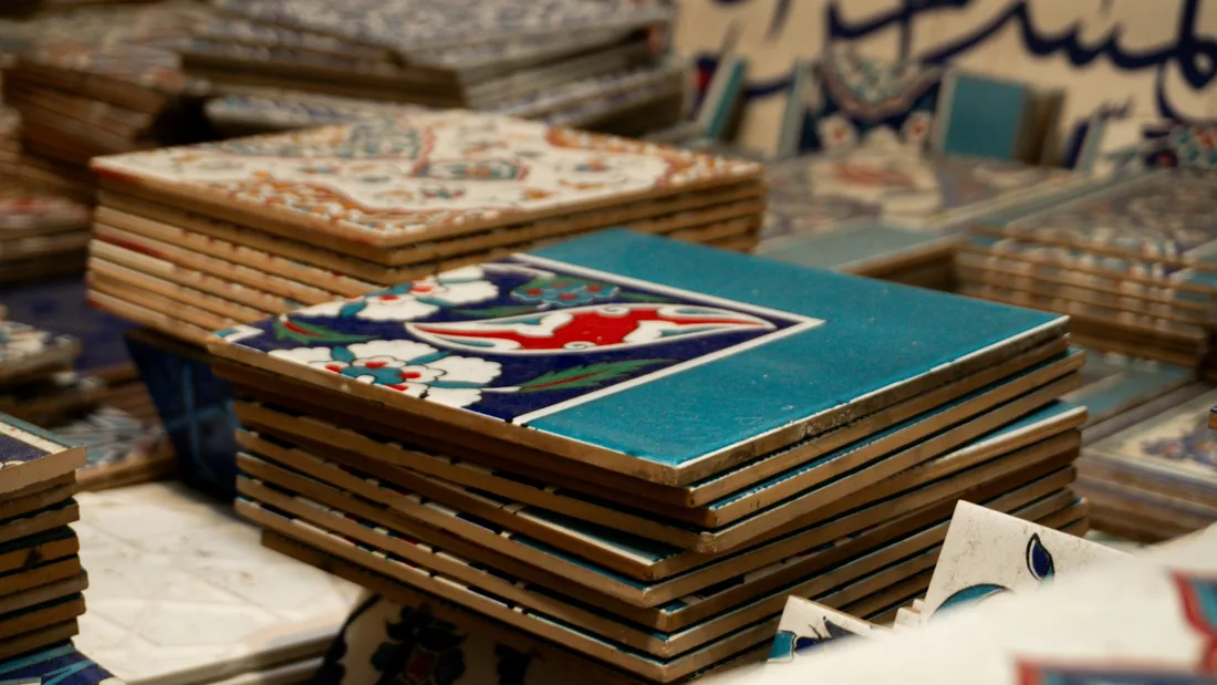 Pilas de azulejos pintados a mano con motivos florales y geométricos, apilados por tandas sobre una mesa de taller
